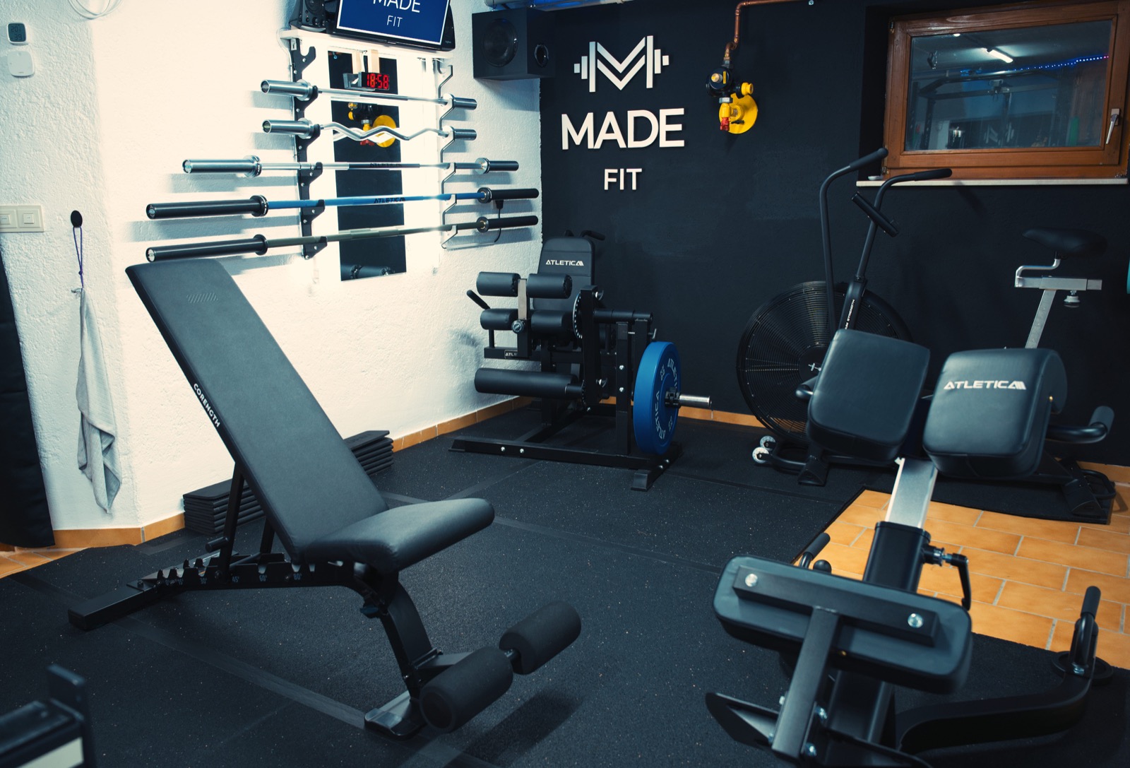 Wide view of the Made Fit home gym with bench, bike, and barbell wall